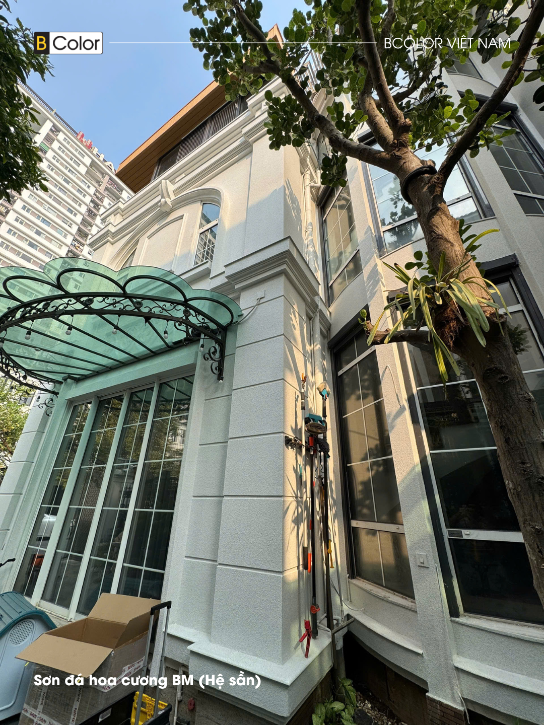 Mặt đứng sơn đá sáng màu cạnh mái kính và hệ khung đỡ sẫm của biệt thự Embassy